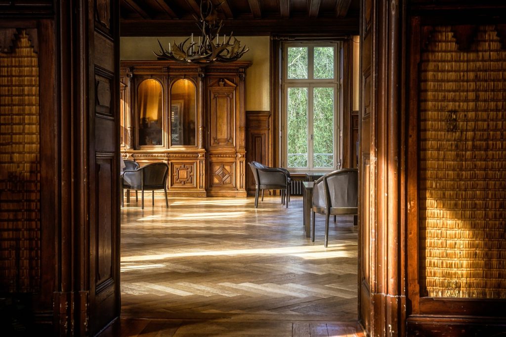 Elegant wood-panelled room with vintage furniture, large windows, and natural light streaming onto the wooden floor